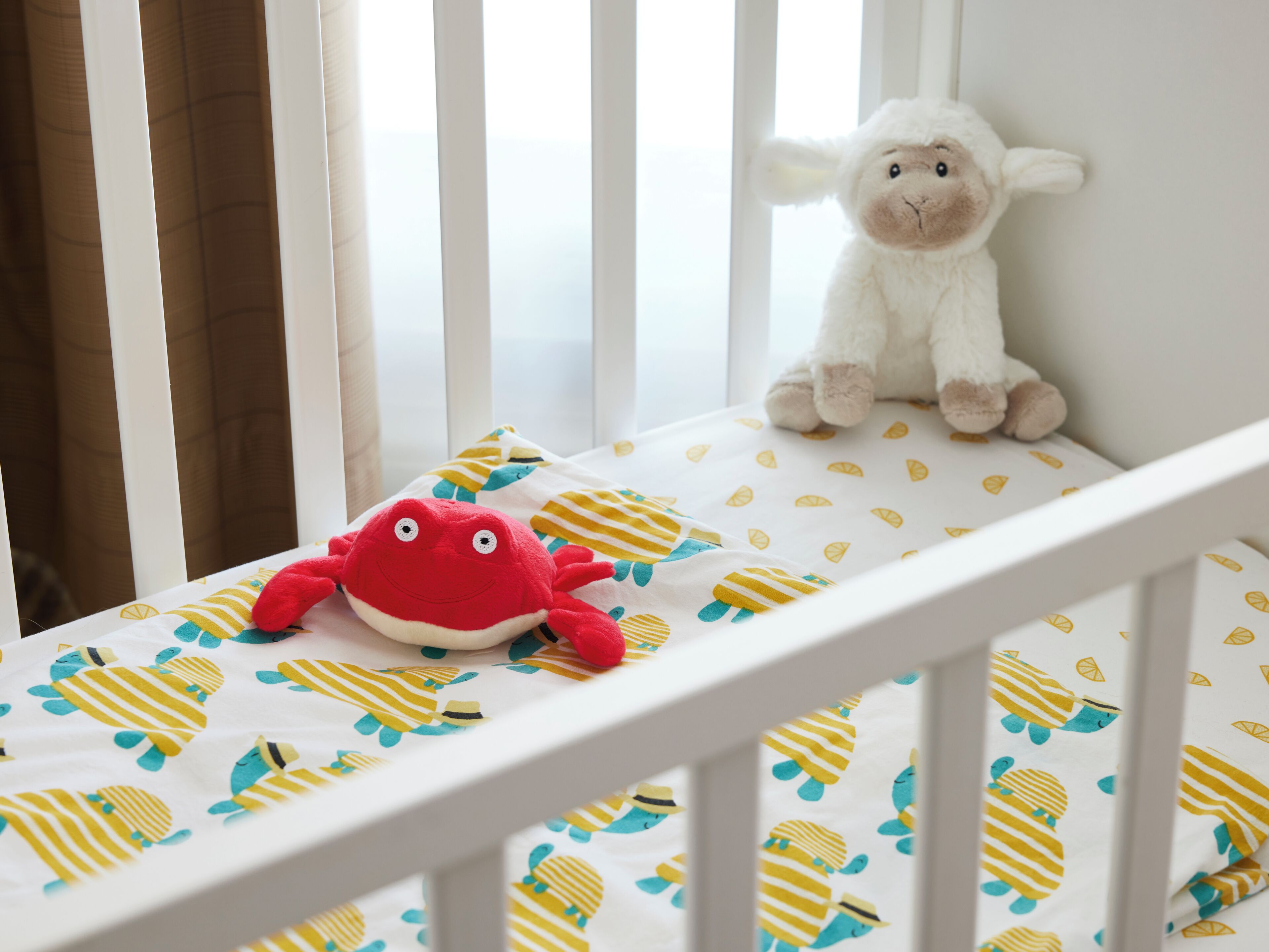 Una cuna con estructura blanca, sábanas estampadas y dos peluches.