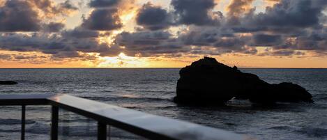 A sunset over the ocean with a rock formation in the distance.