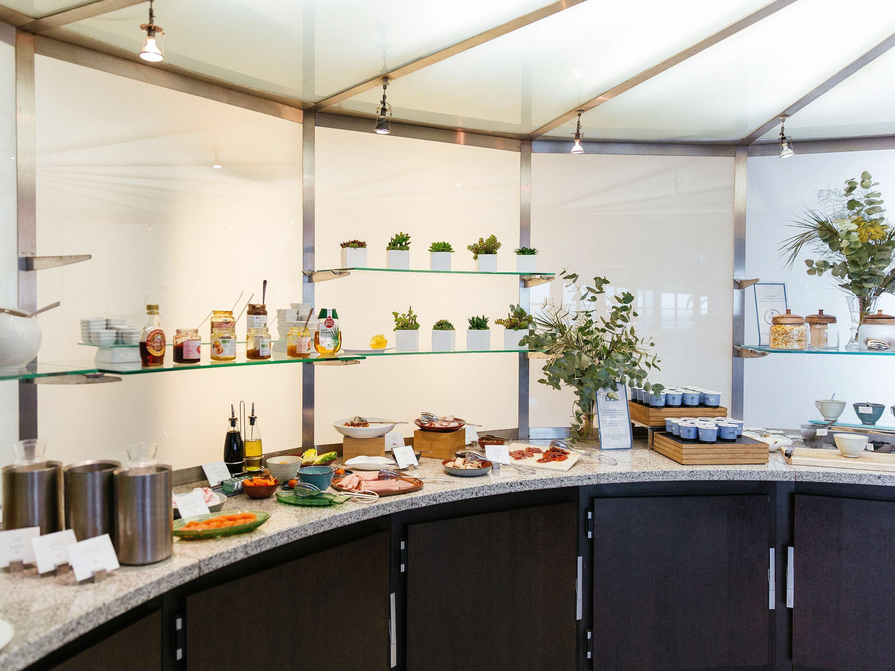 Una cocina moderna con estantes de vidrio que exhiben condimentos y pequeñas plantas, una encimera de granito con alimentos y armarios oscuros.