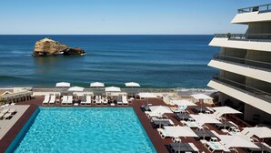 Zona de piscina amb gandules i ombrelles, amb vista al mar i una roca.