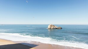 Una platja amb cel blau, una roca a l'aigua i ones que arriben a la riba.