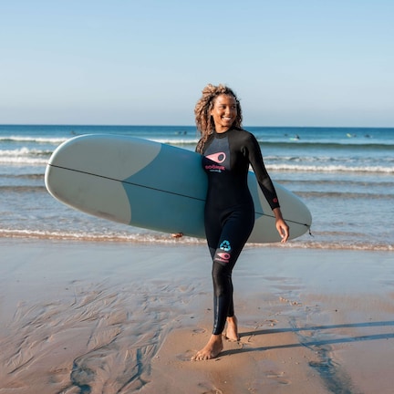 A person in a wetsuit holding a surfboard on a beach.