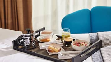 A breakfast tray on a bed with a cup of coffee, a glass of juice, a bowl of cereal, and a slice of toast.