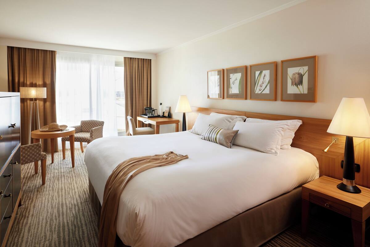 Una habitación de hotel con una cama grande, un escritorio, una silla, una lámpara e impresiones botánicas enmarcadas en la pared.