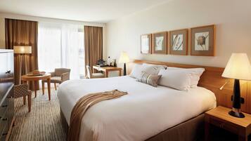 A hotel room with a large bed, a desk, a chair, a lamp, and framed botanical prints on the wall.