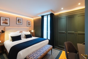 A hotel room with a large bed, a bench, a desk, and a wardrobe.