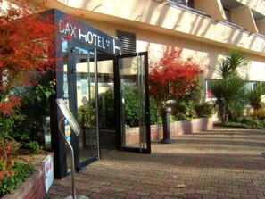 The exterior of a hotel with a glass entrance, a sign above the door, and surrounding greenery. - Dax Hôtel (Dax)