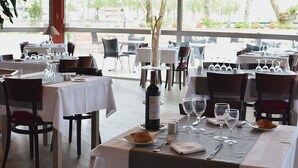 A restaurant with tables set for dining, wine glasses, and a bottle of wine on the table. - Dax Hôtel (Dax)