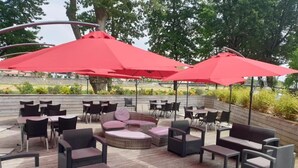 An outdoor patio with wicker furniture, red umbrellas, and a view of the surrounding area. - Dax Hôtel (Dax)