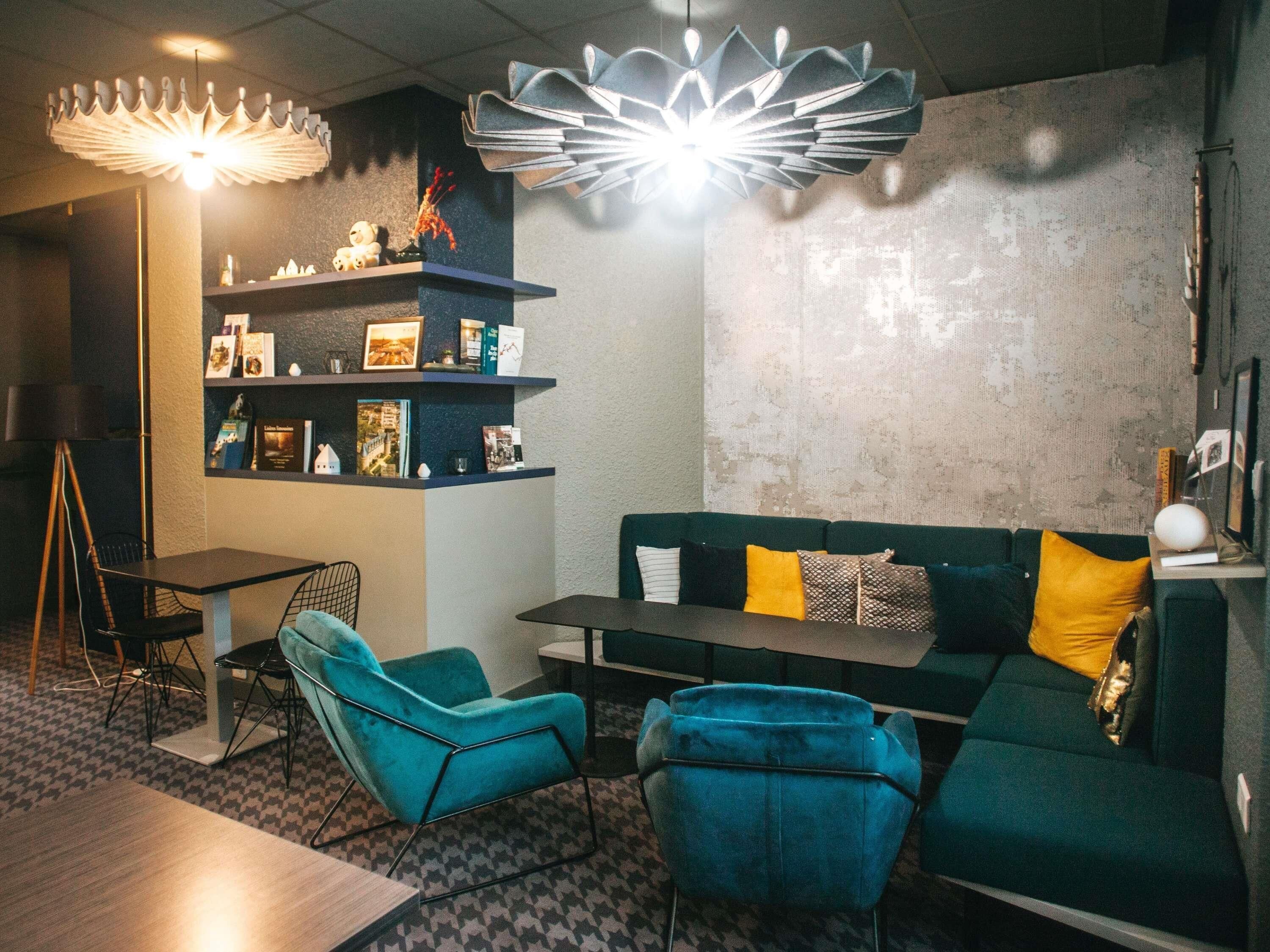 A modern living room with teal chairs, a green sofa, a bookshelf, and a unique ceiling light fixture.