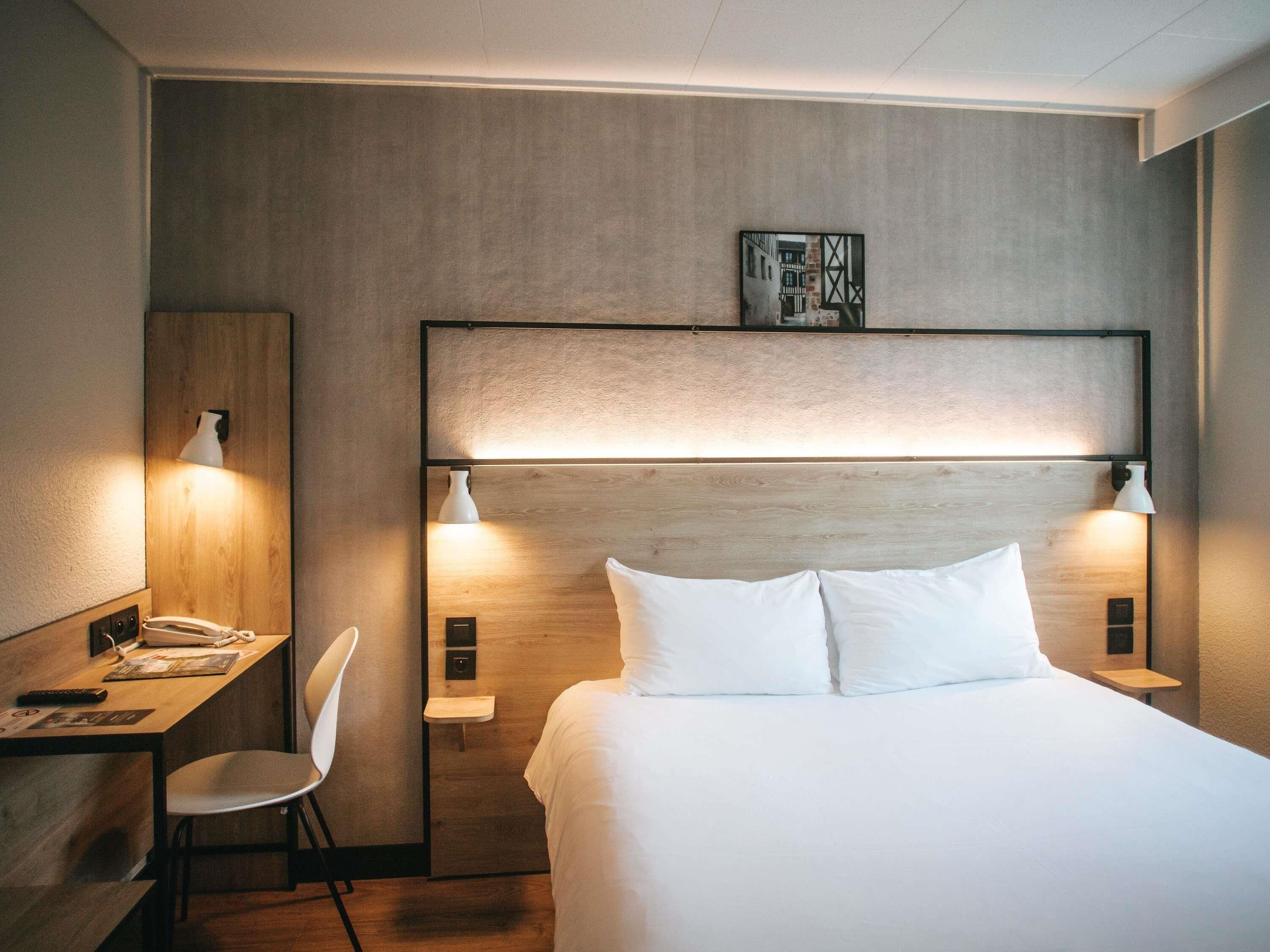 Une chambre d’hôtel avec un lit, des lampes de chevet, un bureau avec un téléphone et une chaise.