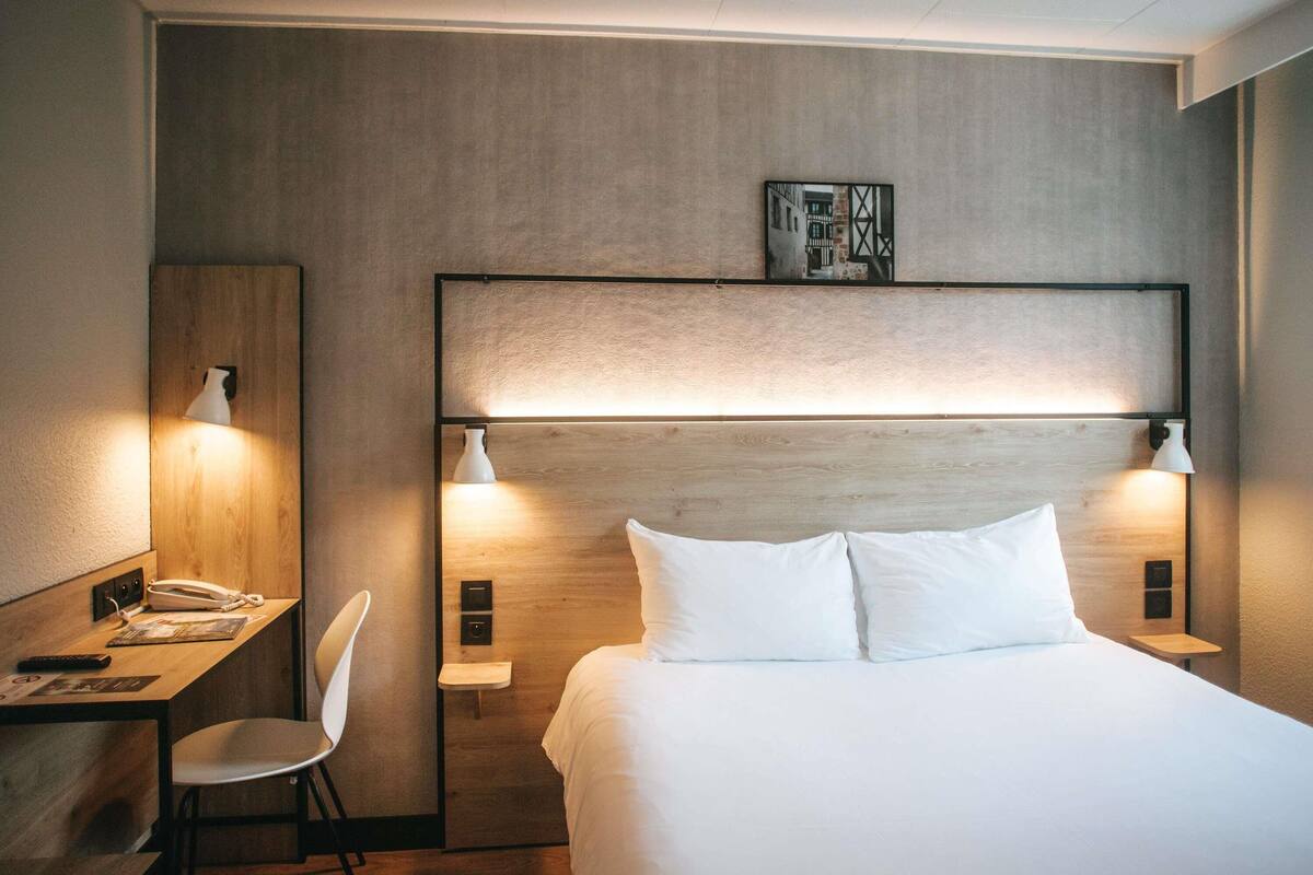 A hotel room with a bed, bedside lamps, a desk with a phone, and a chair.