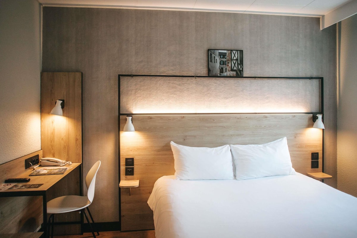 Habitación de hotel con cama, lámparas de noche, escritorio con teléfono y una silla.