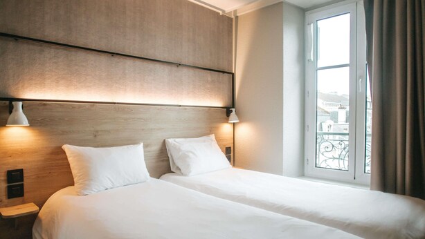 Et hotelværelse med to senge, et træhovedgærde, sengeborde med lamper, et vindue med udsigt og en balkon.