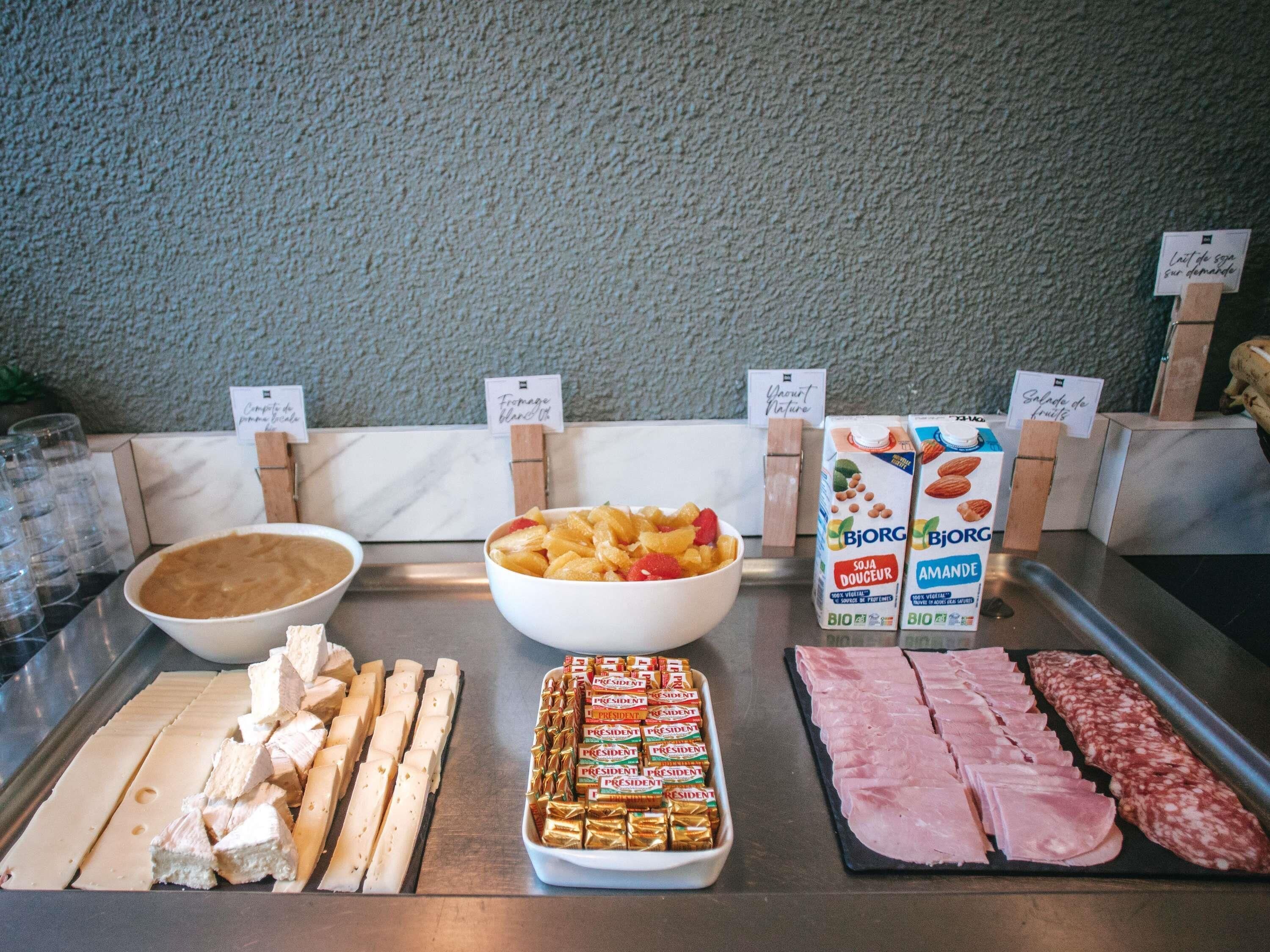 A buffet with various food items including a bowl of fruit, cheese, ham, and packaged snacks.