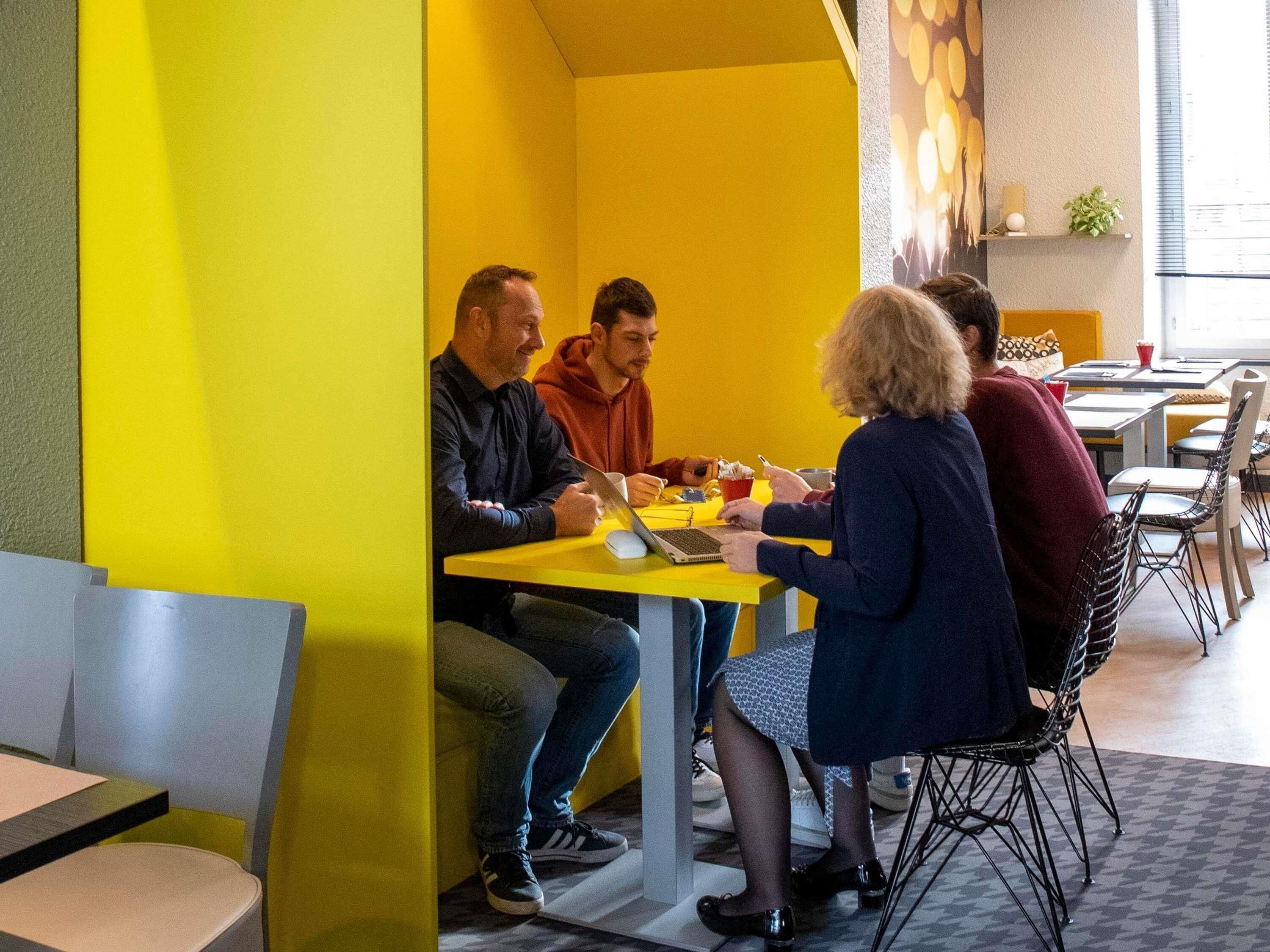 A group of people seated around a yellow table in a brightly lit room with a modern design.