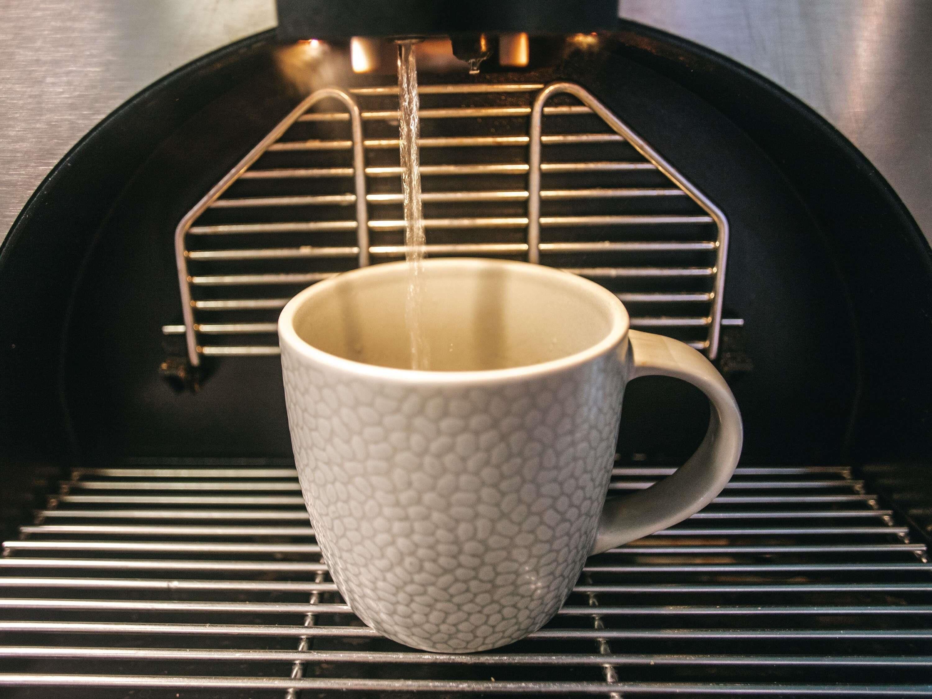 Una taza de café sobre un porta tazas metálico dentro de una máquina de café.