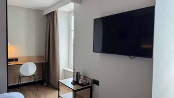 Une chambre d’hôtel avec un lit, un bureau, une chaise, une télévision et une fenêtre avec des rideaux.