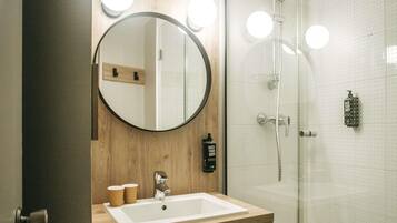 A bathroom with a wooden vanity, a round mirror, a sink, and a glass shower enclosure.