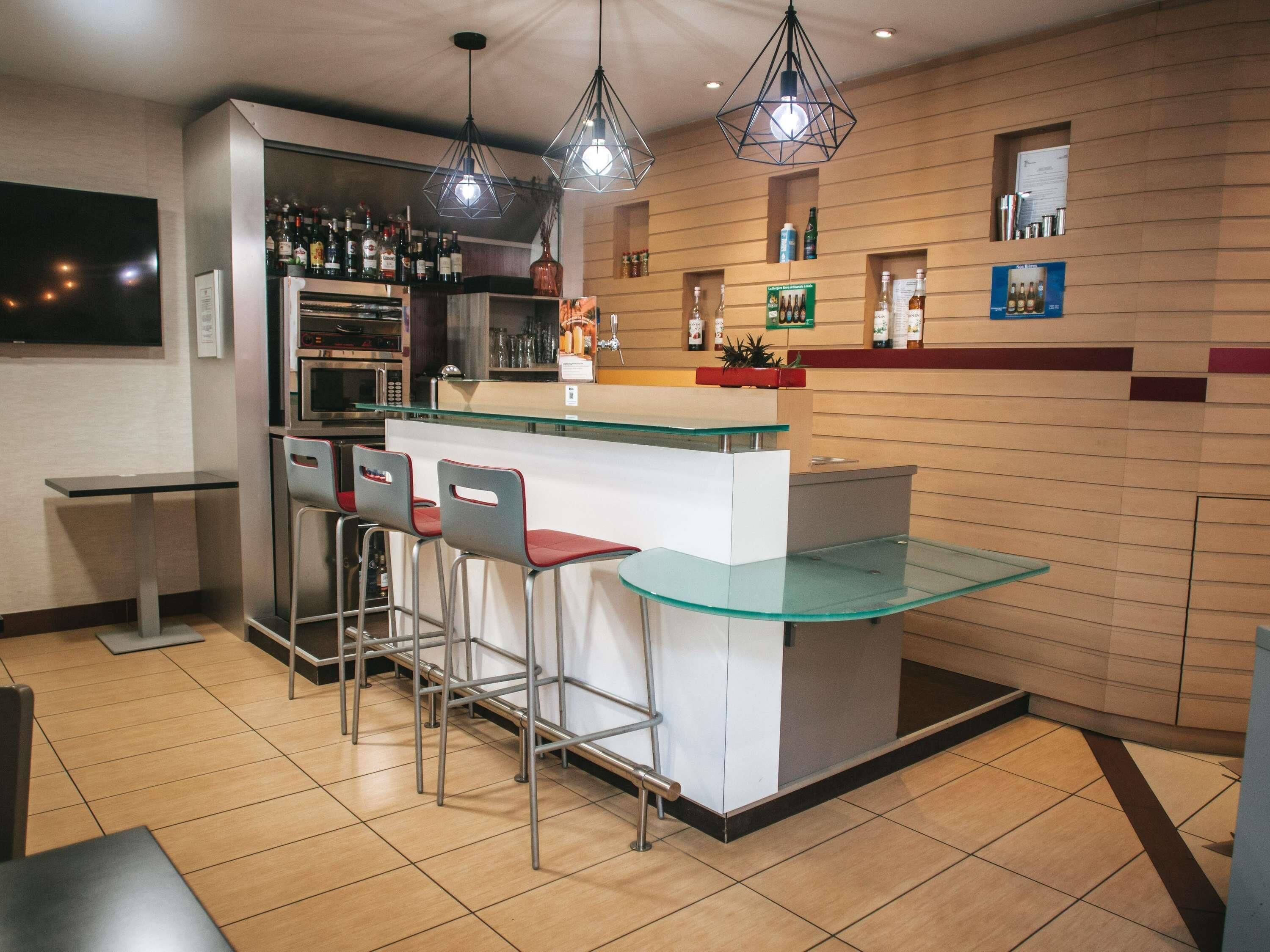Uma área de bar moderna com balcão de vidro, banquetes de metal e iluminação suspensa.