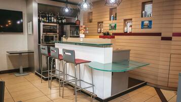 Uma área de bar moderna com balcão de vidro, banquetes de metal e iluminação suspensa.
