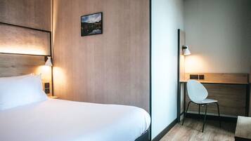 A hotel room with a bed, bedside lamps, a chair, a desk, and a framed picture on the wall.