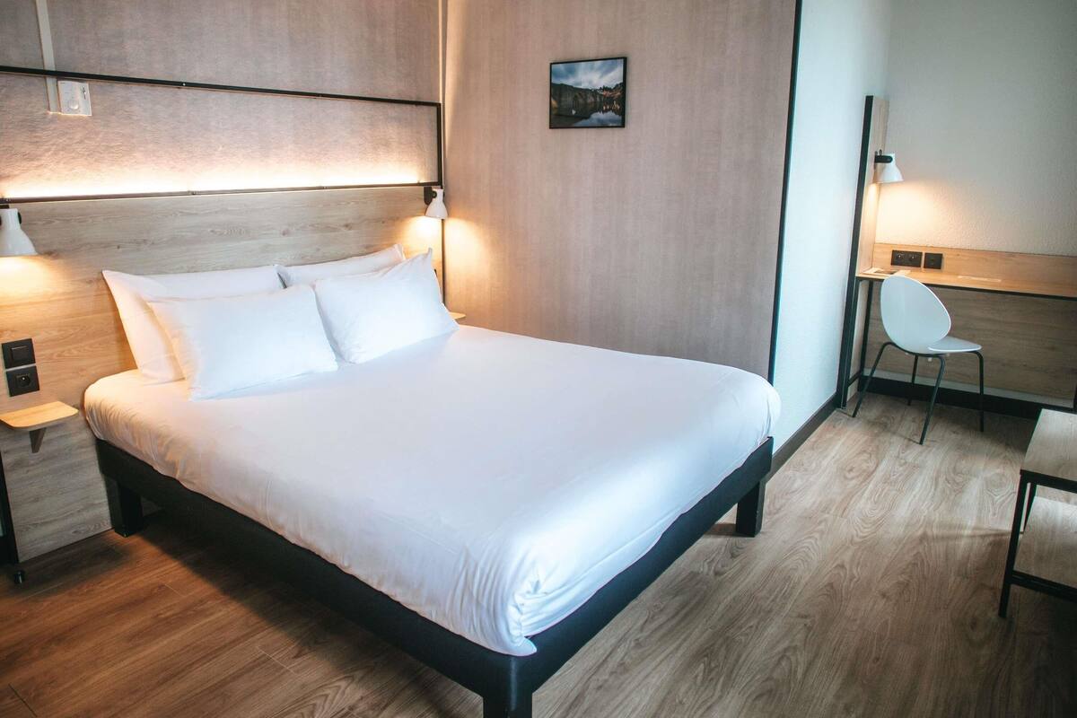 A neatly made bed with white linens, a wooden headboard, and bedside lamps.