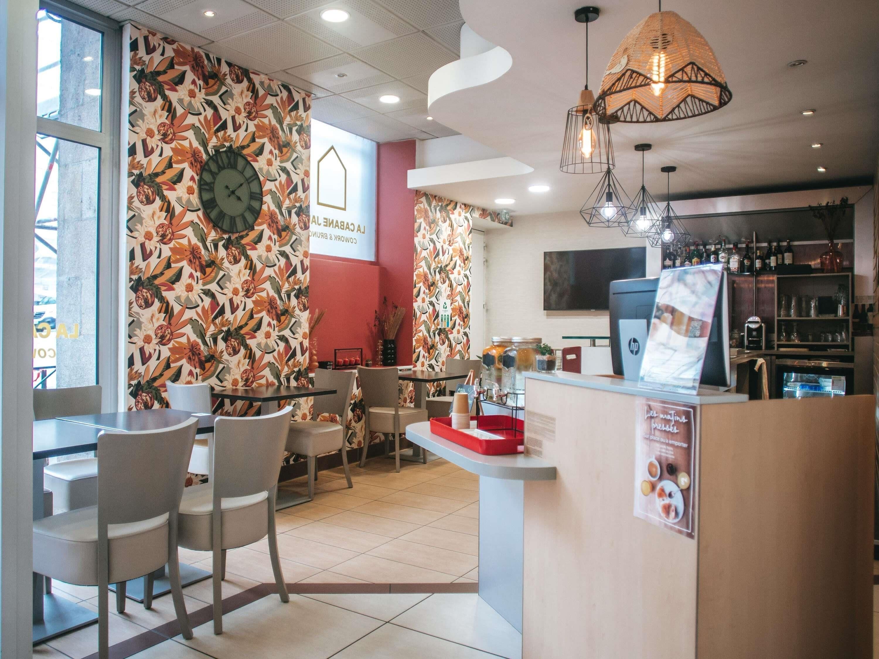Un café avec un mur décoré d’une fresque florale, une horloge et un bar avec des étagères remplies de bouteilles.