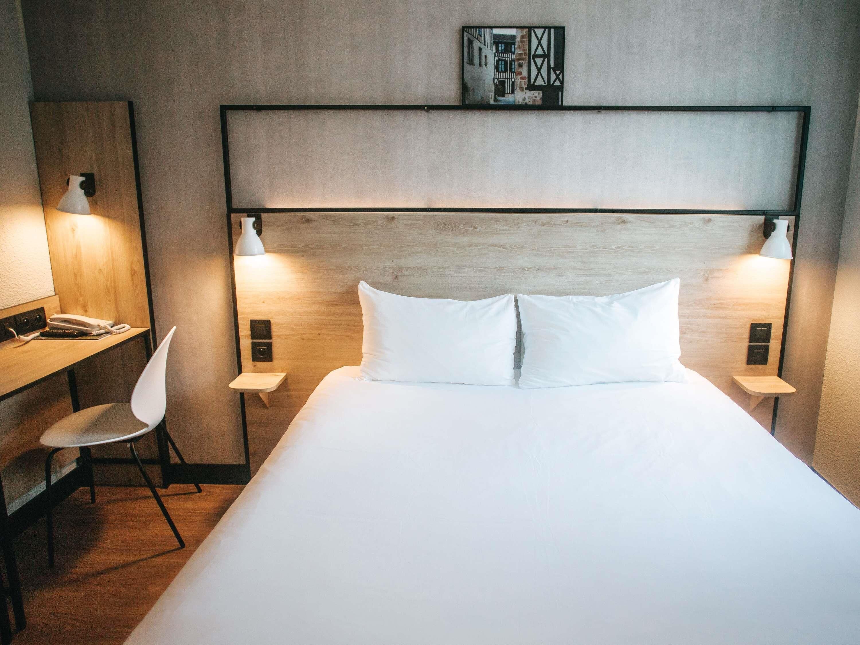 Habitación de hotel con una cama grande, dos lámparas de noche, un escritorio con una silla e imagen colgada en la pared.