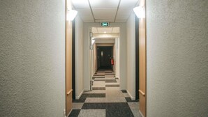 En hotelgang med et ternet gulvtæppe, hvide vægge og en brandslukker til højre.