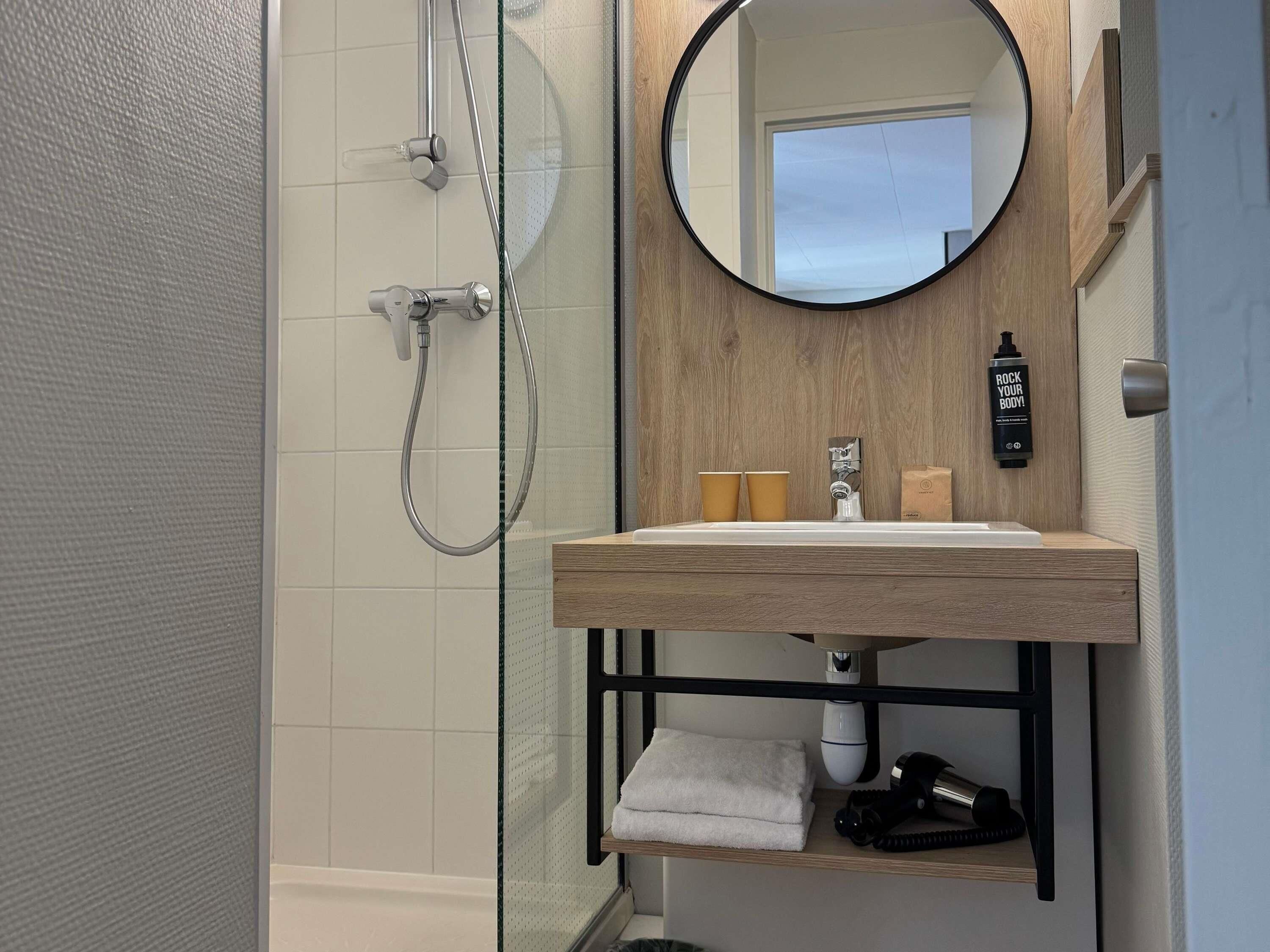 Un baño moderno con cabina de ducha de vidrio, tocador de madera con espejo y un perchero para toallas.