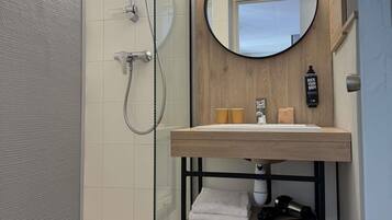 Un baño moderno con cabina de ducha de vidrio, tocador de madera con espejo y un perchero para toallas.