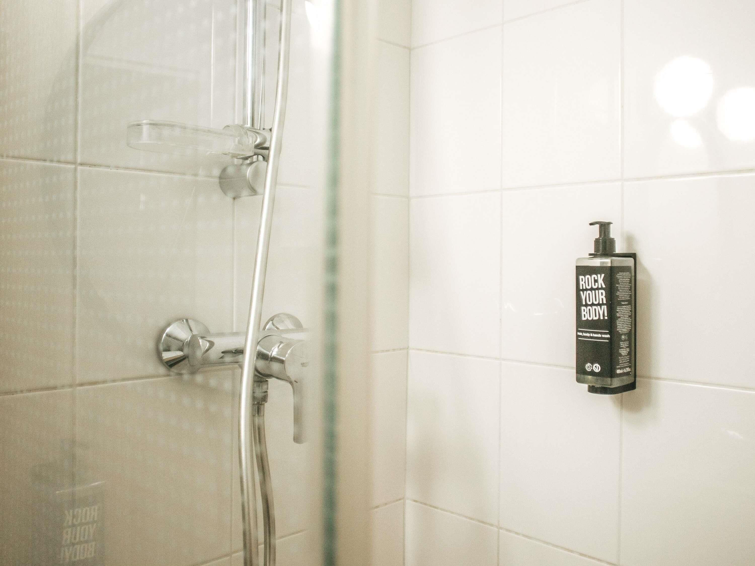 A shower with a glass door, a handheld showerhead, and a bottle of body wash on the wall.