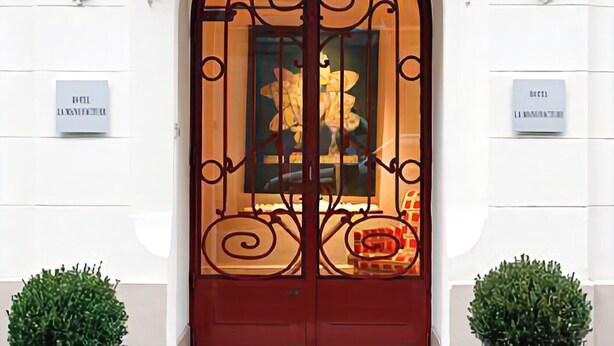 A hotel entrance with a red door, white walls, and decorative moldings. - La Manufacture (Paris)