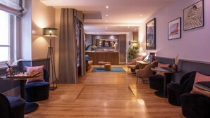 A modern hotel lobby with a wooden floor, seating areas, a reception desk, and artwork on the walls. - La Manufacture (Paris)