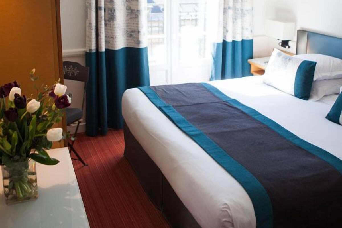 Ein Hotelzimmer mit Bett, Schreibtisch, Stuhl und einem fenster mit Vorhängen.