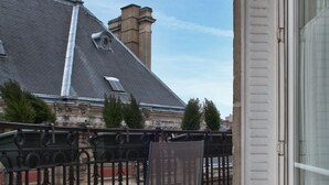 A balcony with a table set for breakfast, a chair, and a view of a building with a grey roof and chimneys. - La Manufacture (Paris)