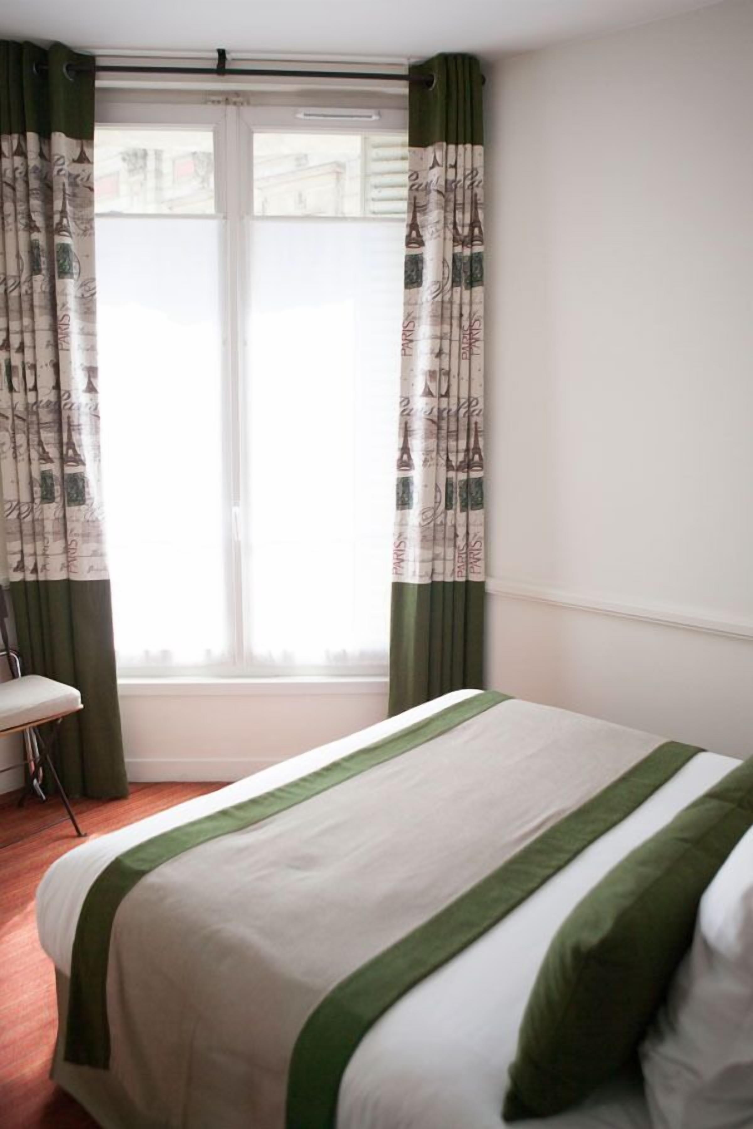A hotel room with a bed, a chair, and a window with curtains.