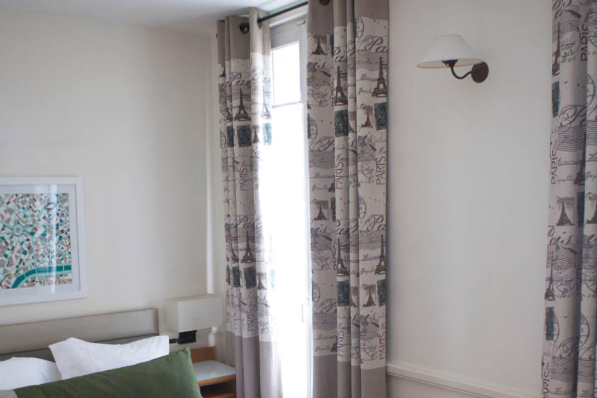 Ein Hotelzimmer mit einem großen Bett, einem Nachttisch, einer Lampe und Vorhängen mit Paris-Design.