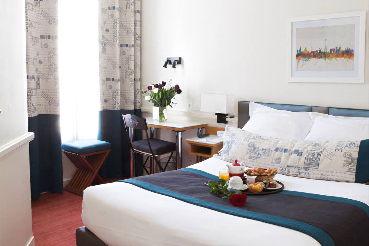 Ein Hotelzimmer mit einem großen Bett, einem Schreibtisch mit Stuhl, einem Flachbildfernseher und einem Frühstückswagen auf dem Bett.