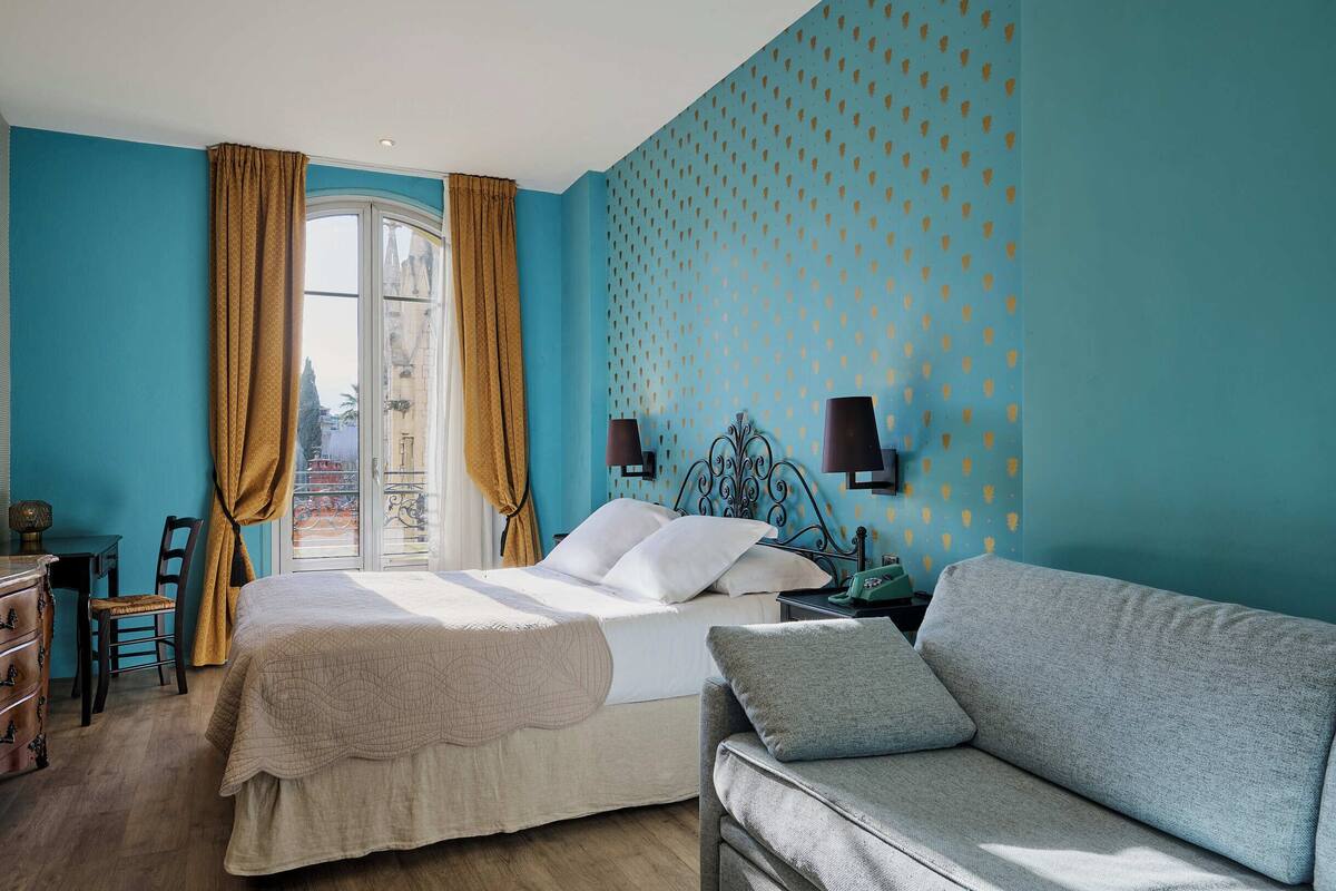 Una habitación de hotel con cama, sofá, escritorio y ventana con cortinas.