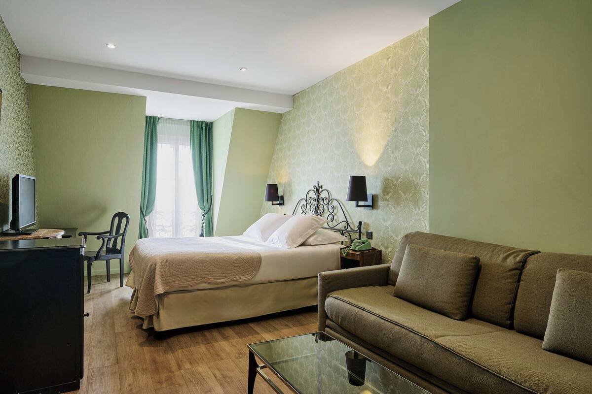 Una habitación de hotel con una cama, un sofá, un escritorio con una computadora y un televisor.