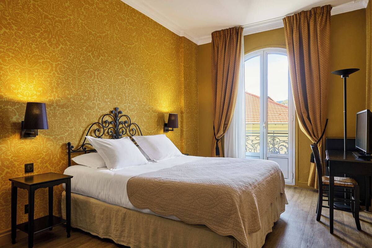 Habitación de hotel con cama, dos lámparas de noche, un escritorio con silla y vistas al exterior.