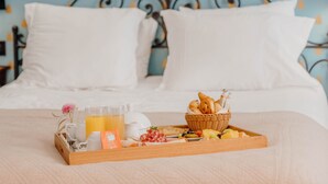 Un plateau de petit-déjeuner joliment préparé, avec du pain, des viennoiseries et des fruits, posé sur un lit doté d’oreillers blancs et d’une tête de lit à motifs bleus.