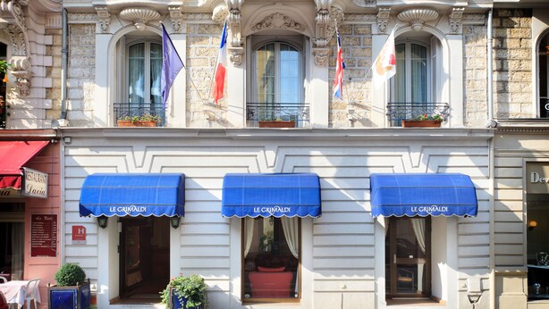 Un bâtiment doté de trois auvents portant l’inscription « LE CRIMALDI », de balcons ornés de plantes en pot et de drapeaux.
