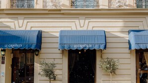 La façade d’un hôtel, ornée de détails architecturaux complexes, de nombreux drapeaux et de plusieurs auvents.
