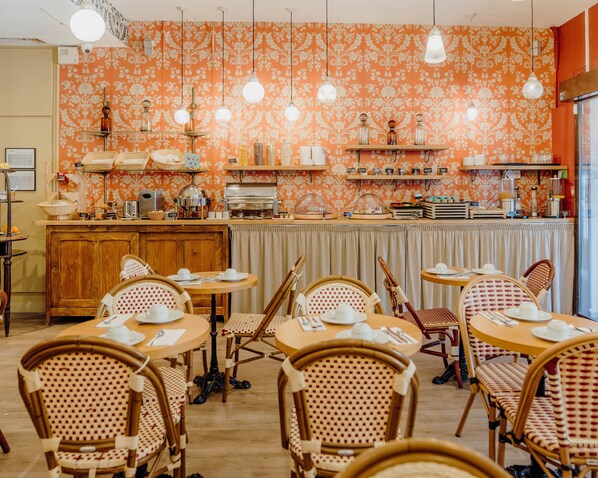 A restaurant with a retro orange floral wallpaper, wooden tables and chairs, and hanging pendant lights.