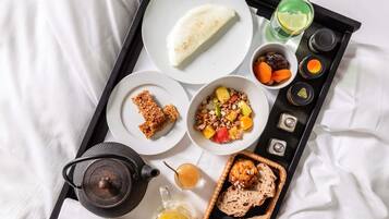 A tray with breakfast items including bread, fruit, and a drink, on a bed.