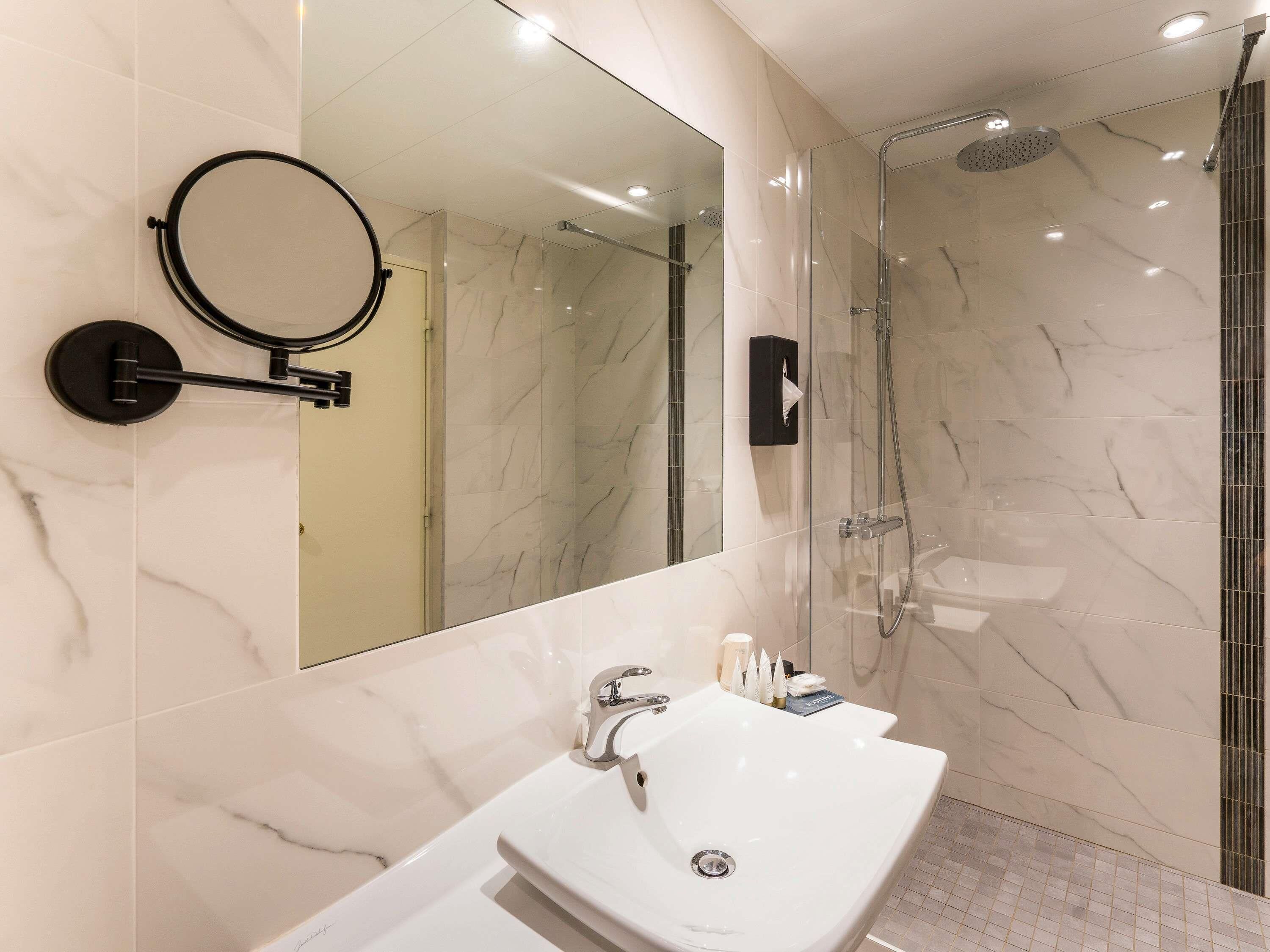 A modern bathroom with a large mirror, a sink, and a shower area.