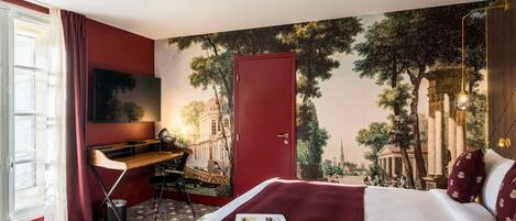 Habitación de hotel con cama, escritorio, silla, televisor y un mural de un edificio histórico.